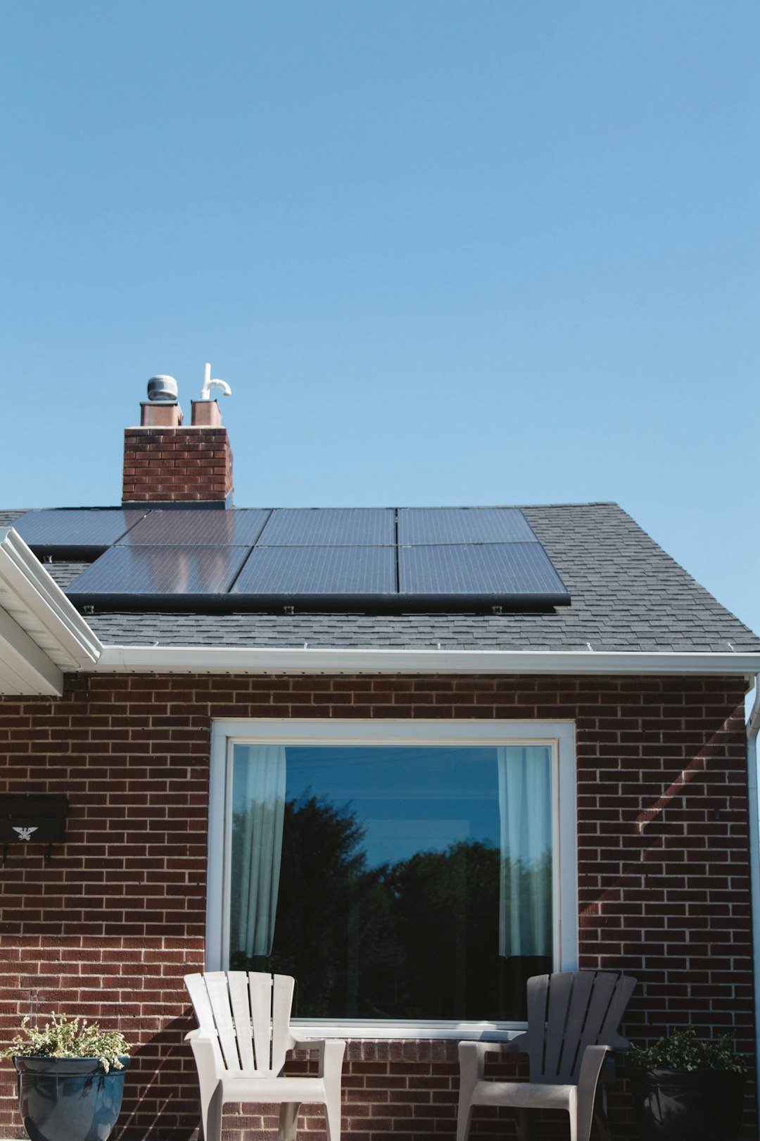 service-02 Vivint Solar - Solar Panels on roof of brick home with window and Adirondack chairs.